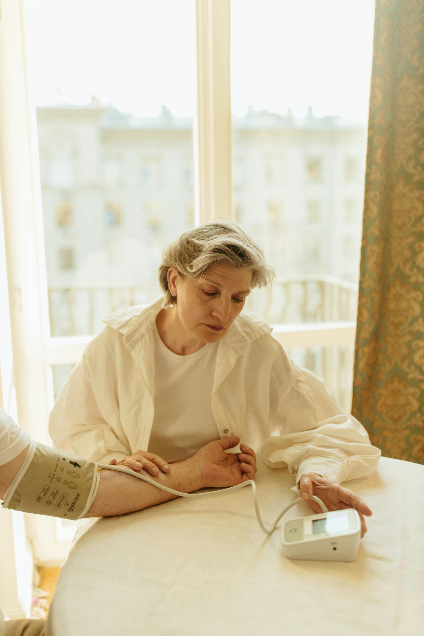 Senior woman checks blood pressure with a monitor by a window. Health care at home.